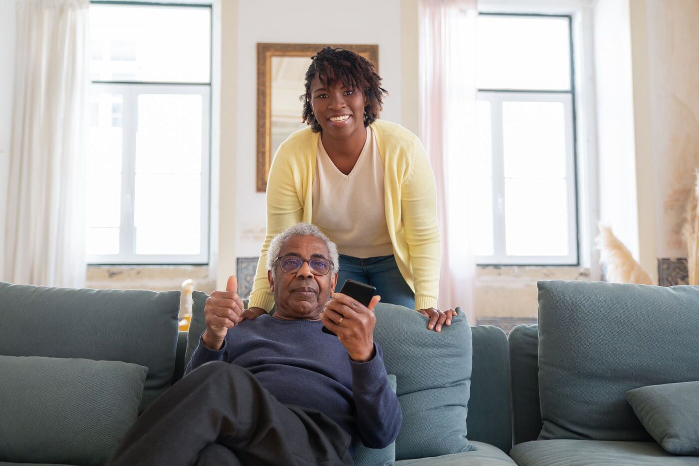 A smiling carer with an older man relaxing on his sofa at home