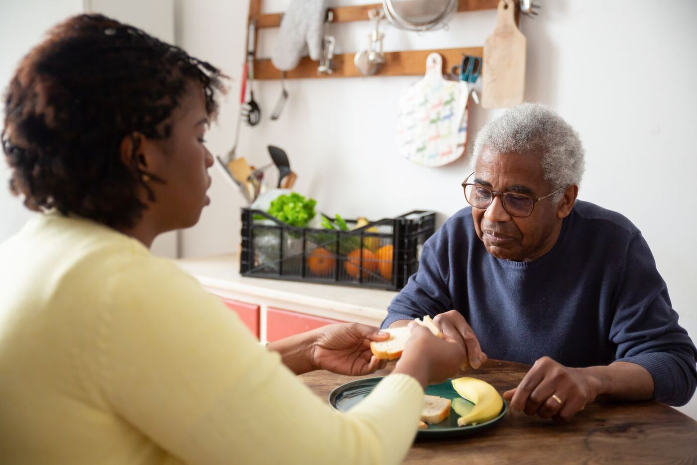 A carer sharing a meal with an older man at his kitchen table